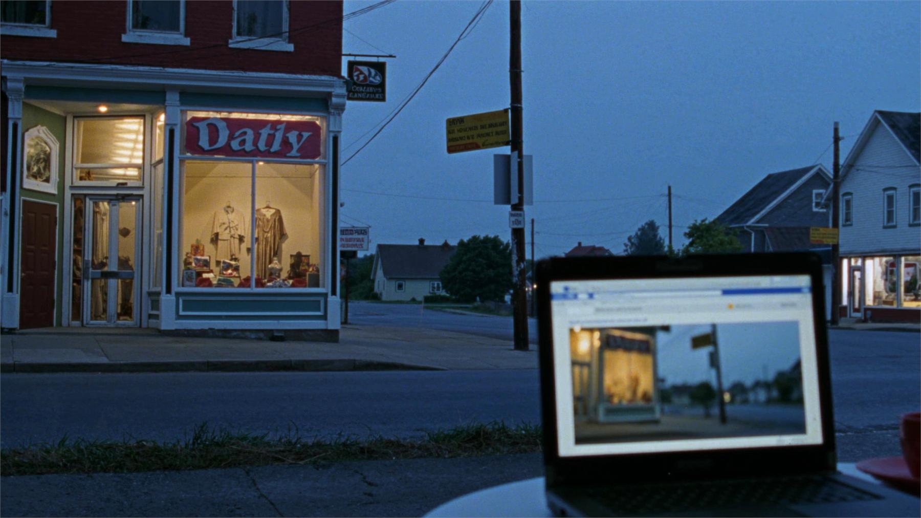 Une devanture de commerce éclairée au crépuscule, et un ordinateur portable qui affiche la même vitrine en ligne